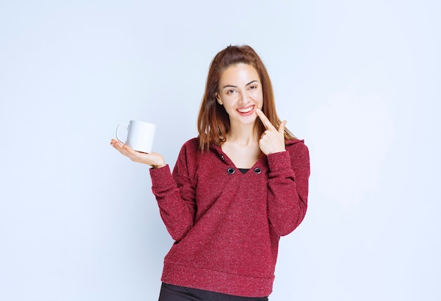 Jeune femme en veste rouge tenant une tasse de café blanche et a l'air réfléchie