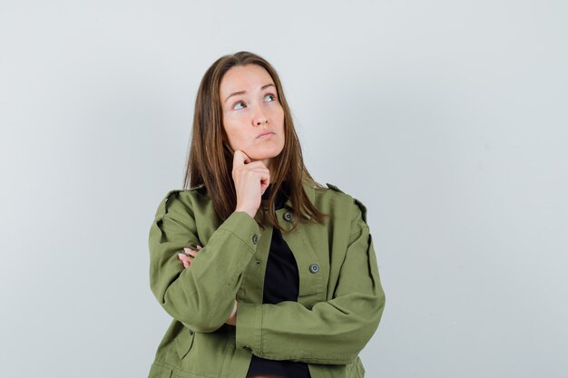 Jeune femme en veste verte en détournant les yeux et regardant pensif, vue de face.