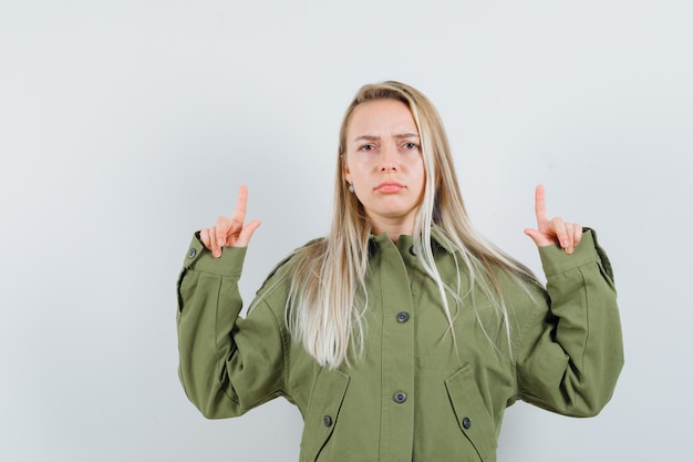 Jeune femme en veste verte pointant vers le haut et à la vue de face, mécontent.