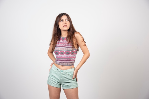 Jeune femme en vêtements d'été posant sur un mur gris.