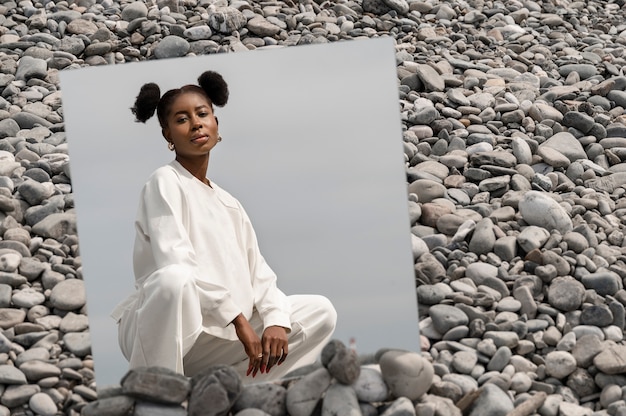 Jeune femme vêtue de blanc posant avec miroir dans les rochers