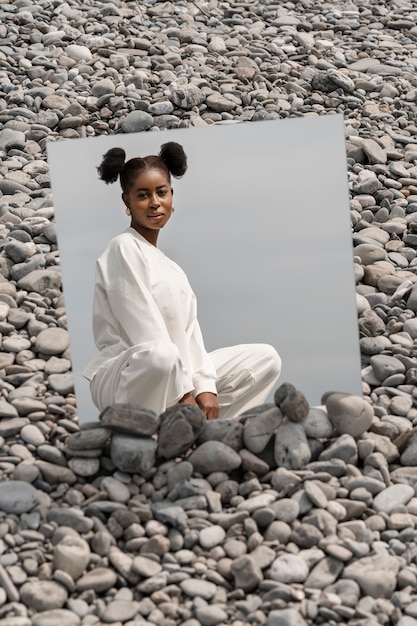 Photo gratuite jeune femme vêtue de blanc posant avec miroir dans les rochers