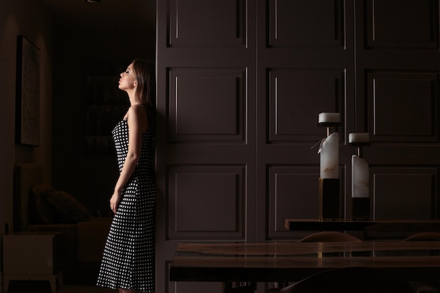 Photo gratuite jeune femme vêtue d'une robe et debout sur une pièce sombre et élégante