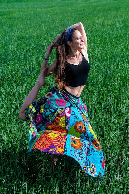 Photo gratuite jeune femme vêtue d'une robe à fleurs méditant dans le champ d'herbe