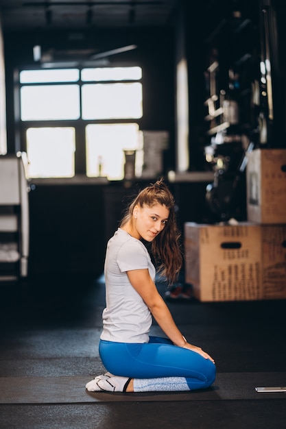 Jeune femme de yoga à genoux sur le sol. Sur fond sombre.