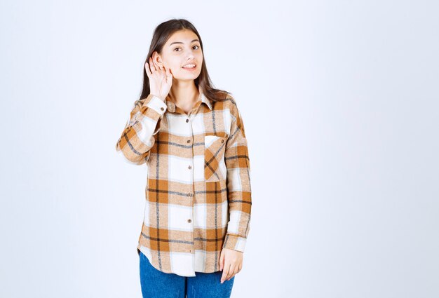 Jeune fille adorable dans des vêtements décontractés écoutant quelque chose sur un mur blanc.