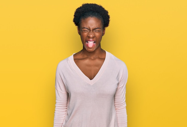 Jeune fille afro-américaine portant des vêtements décontractés tirant la langue heureuse avec le concept drôle d'émotion d'expression