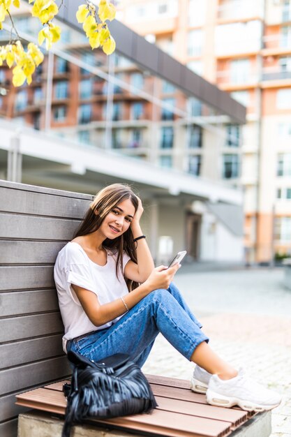 Jeune fille à l'aide d'un téléphone intelligent et envoyer des SMS assis sur un banc d'un parc urbain