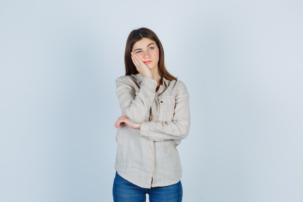 Jeune Fille Appuyée Sur La Joue De La Paume, Pensant à Quelque Chose En Chemise Beige, Jeans Et Regardant Pensive, Vue De Face.