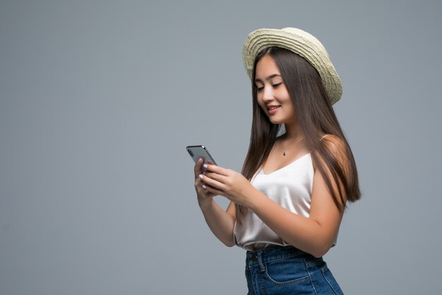 Jeune fille asiatique avec un chapeau de paille utiliser le téléphone sur fond gris