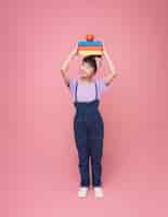 Photo gratuite une jeune fille asiatique souriante ou une écolière élémentaire tenant des livres sur la tête