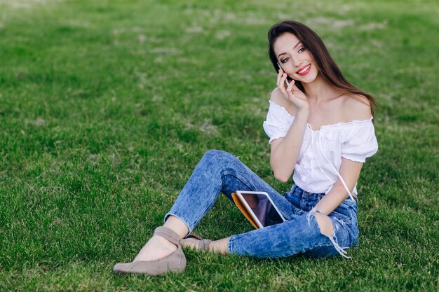 Jeune fille assise dans un parc de parler au téléphone tout en souriant