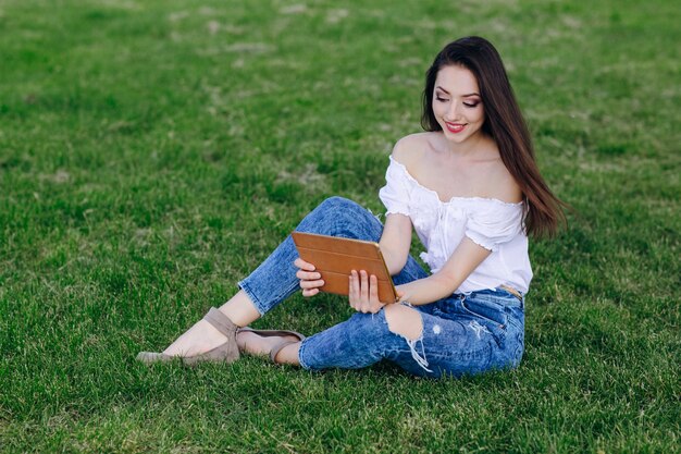 Jeune fille assise dans un parc en souriant tout en regardant un comprimé orange