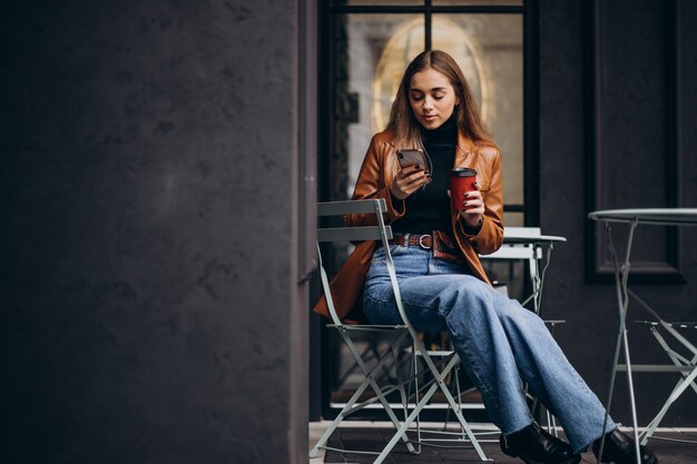 Jeune fille assise à l'extérieur du café et boire du café