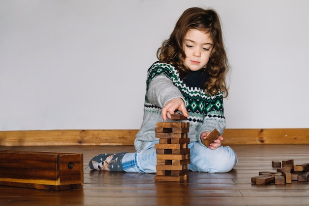 Jeune fille assise sur le plancher en bois empilant le bloc