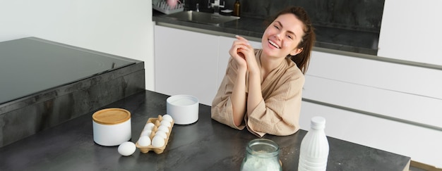 Photo gratuite une jeune fille attrayante et joyeuse qui fait de la pâte dans la cuisine, qui tient un livre de recettes, qui a des idées.