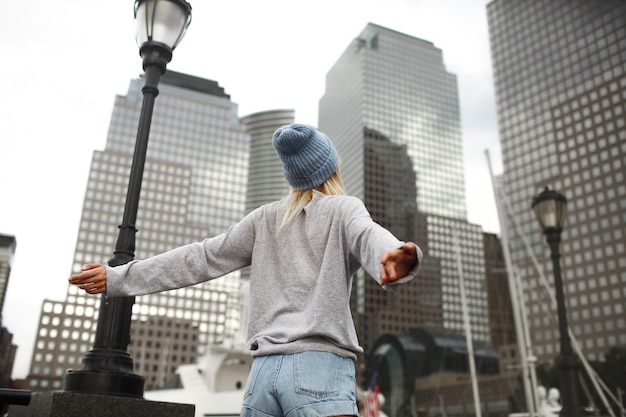 Jeune fille au chapeau bleu et chandail gris se dresse dans la rue avec des gratte-ciel