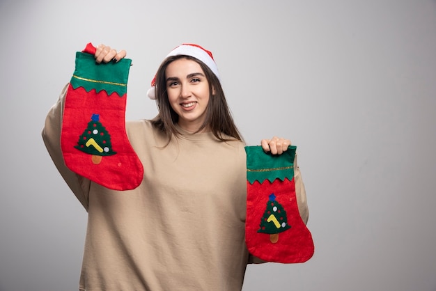 Photo gratuite jeune fille au chapeau du père noël tenant deux chaussettes de noël.