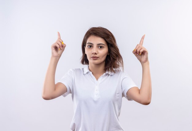 Jeune fille aux cheveux courts portant un polo blanc à la confiance en pointant avec l'index vers le haut