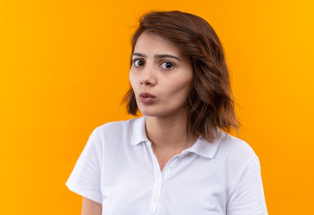 Jeune fille aux cheveux courts portant un polo blanc regardant la caméra confuse et très anxieuse