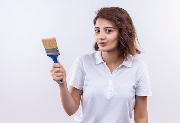 Photo gratuite jeune fille aux cheveux courts portant un polo blanc tenant un pinceau à la confiance