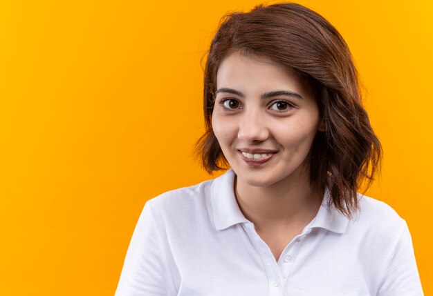 Jeune fille aux cheveux courts portant un polo regardant la caméra avec le sourire sur le visage