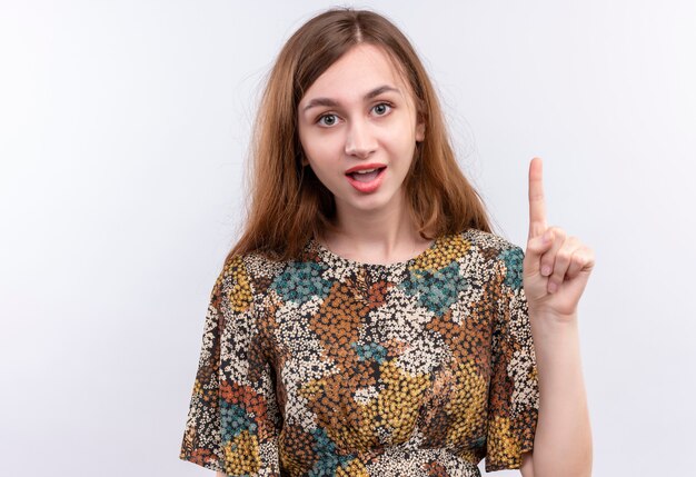 Jeune fille aux cheveux longs portant une robe colorée pointant l'index vers le haut d'avertissement