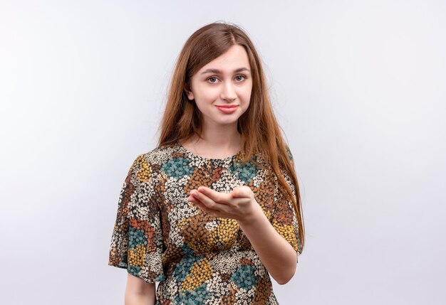 Jeune fille aux cheveux longs portant une robe colorée présentant le bras de sa main souriant confiant