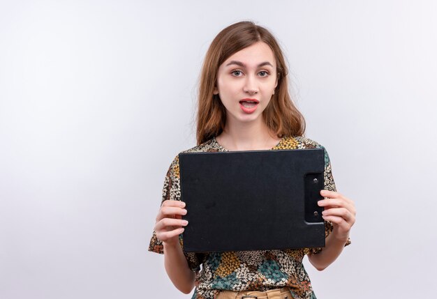 Photo gratuite jeune fille aux cheveux longs portant une robe colorée tenant le presse-papiers en regardant la caméra en souriant heureux et positif