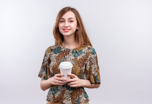 Jeune fille aux cheveux longs portant une robe colorée tenant une tasse de café souriant confiant