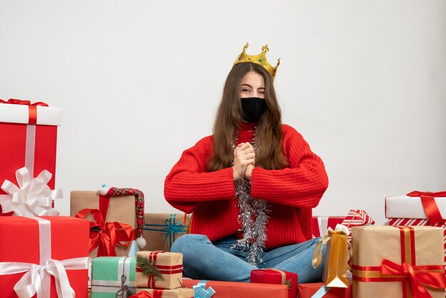 Jeune fille aux yeux clignés assis autour de cadeaux avec masque noir sur blanc