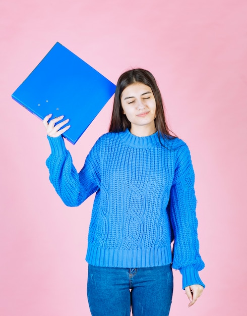 jeune fille aux yeux fermés tenant un dossier bleu sur rose.