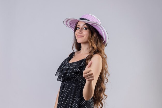 Jeune fille belle voyageur en chapeau d'été regardant la caméra heureux et positif souriant joyeusement montrant les pouces vers le haut debout sur fond blanc