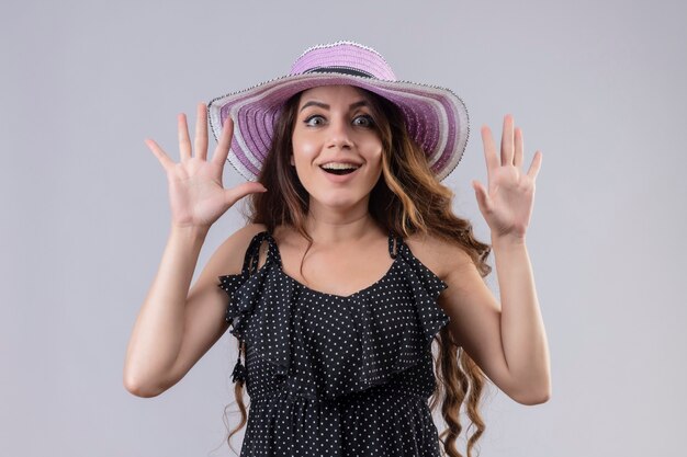 Jeune fille belle voyageur en robe à pois en chapeau d'été debout avec les mains levées en reddition surpris et étonné sur fond blanc