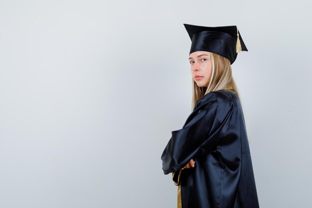 Jeune fille blonde debout avec les bras croisés en uniforme diplômé et à l'air confiant. .