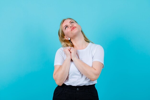 Jeune fille blonde est à la recherche en tenant les mains ensemble sur l'épaule sur fond bleu