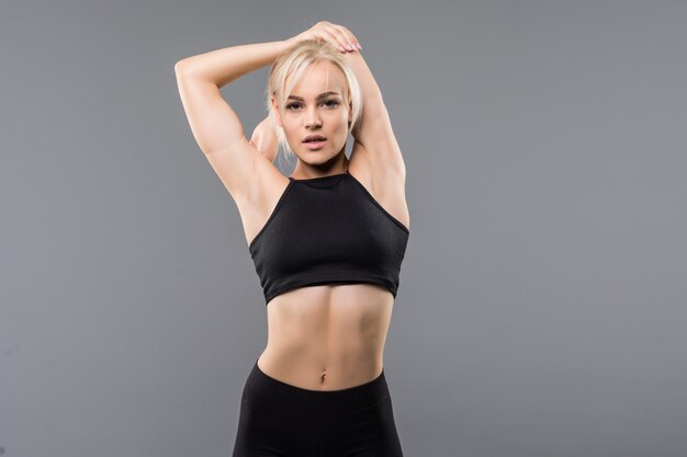 Jeune fille blonde fit sportive femme en vêtements de sport noir démostrate son fort étirement du corps musclé