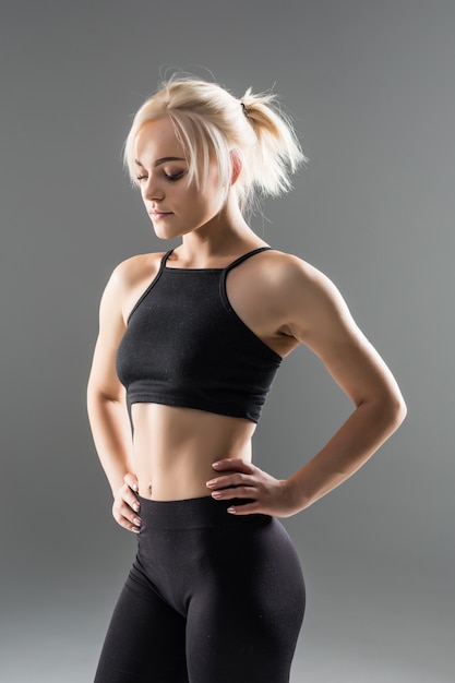 Jeune fille blonde fit sportive femme en vêtements de sport noir démostrate son fort étirement du corps musclé