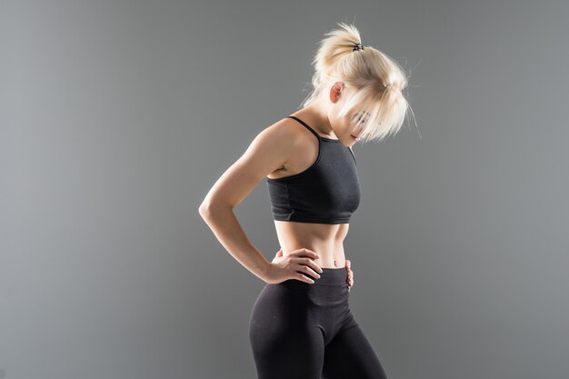 Jeune fille blonde fit sportive femme en vêtements de sport noir démostrate son fort étirement du corps musclé