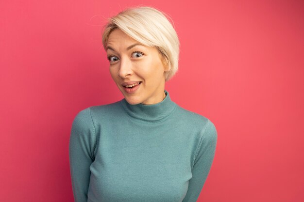 Jeune fille blonde impressionnée à la recherche d'isolement sur le mur rose avec espace de copie