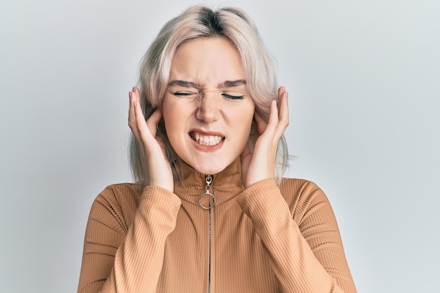 Photo gratuite jeune fille blonde portant des vêtements décontractés couvrant les oreilles avec les doigts avec une expression agacée pour le bruit de la musique forte concept sourd