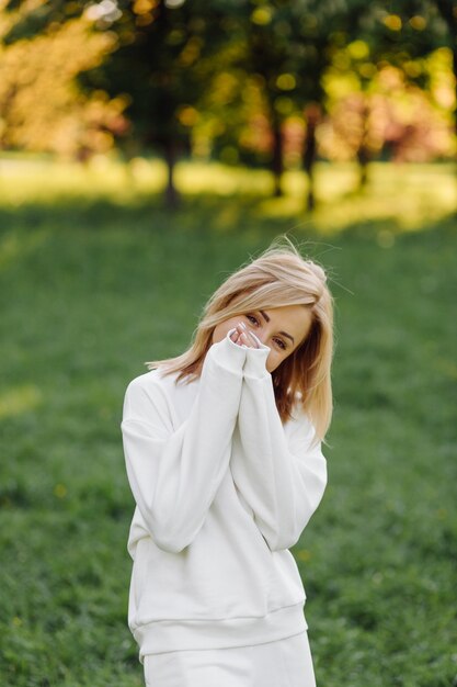 Jeune fille blonde porte un sweat à capuche blanc souriant et marchant dans les bois