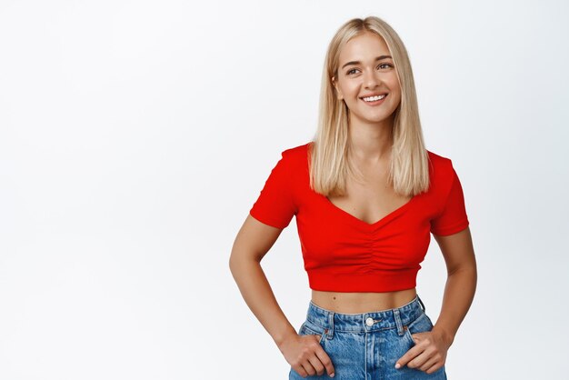 Photo gratuite jeune fille blonde souriante en haut court regardant à gauche debout détendu et heureux fond blanc