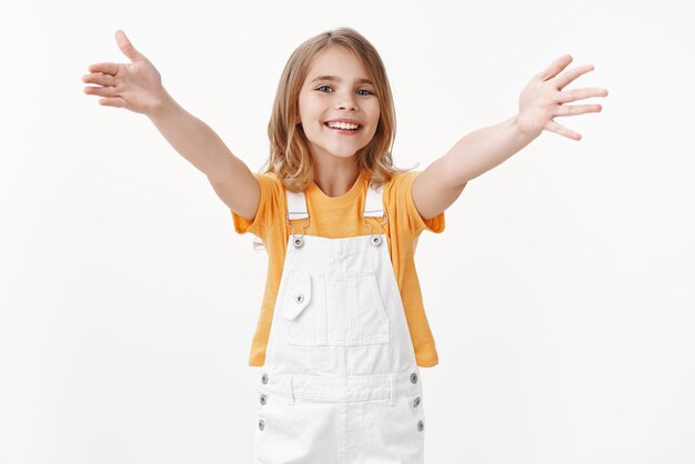 Jeune fille blonde tendre et joyeuse aux yeux bleus, étend les bras et sourit joyeusement, veux câliner, inviter un ami à faire un câlin chaleureux