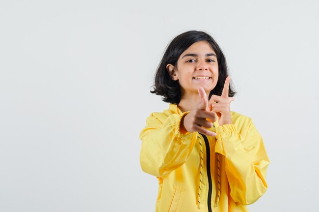 Jeune fille en blouson aviateur jaune pointant la caméra avec l'index et à la recherche de plaisir