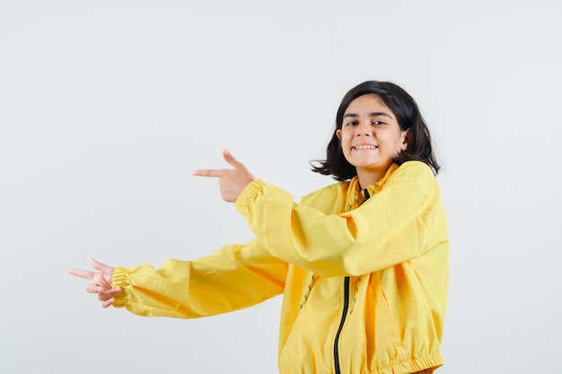Jeune fille en blouson aviateur jaune pointant vers la gauche avec l'index et l'air heureux