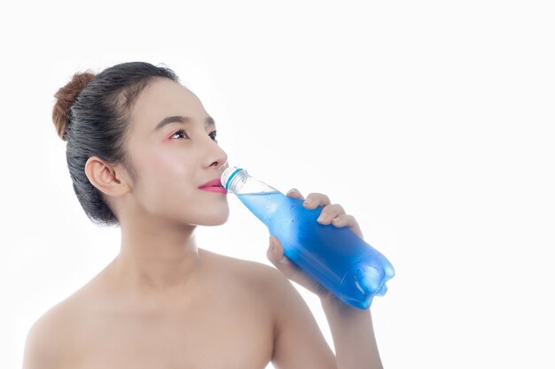 La jeune fille boit de l&#39;eau bleue sur un fond blanc.