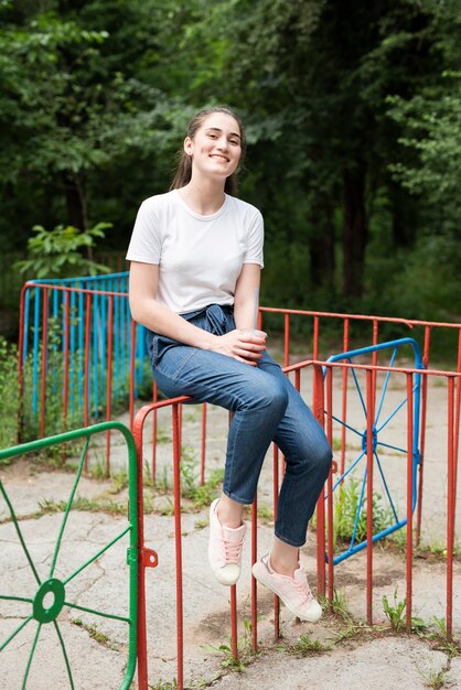 Jeune fille brune assise sur une clôture colorée