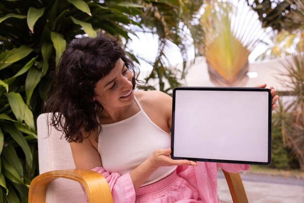 Jeune fille brune caucasienne positive regardant la tenue d'un ipad avec un écran blanc vierge à l'extérieur de l'appareil Concept