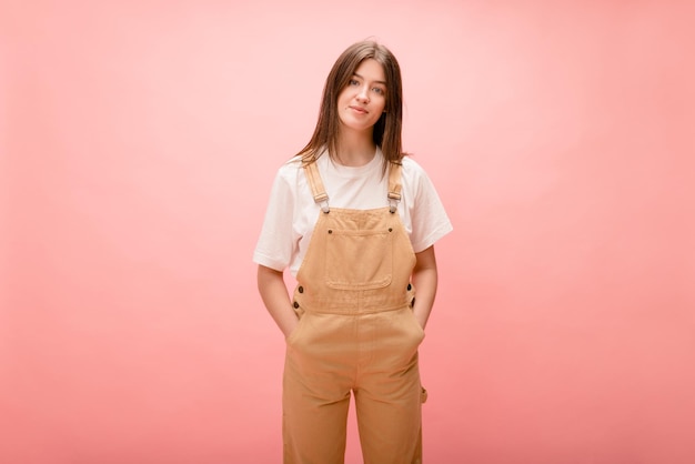 Jeune fille brune élégante à la peau claire tient les mains dans les poches de la salopette sur fond avec place pour le texte Concept de style de vie de loisirs